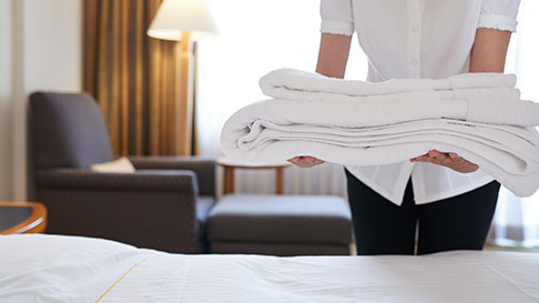 woman holding white towels over a hotel bed